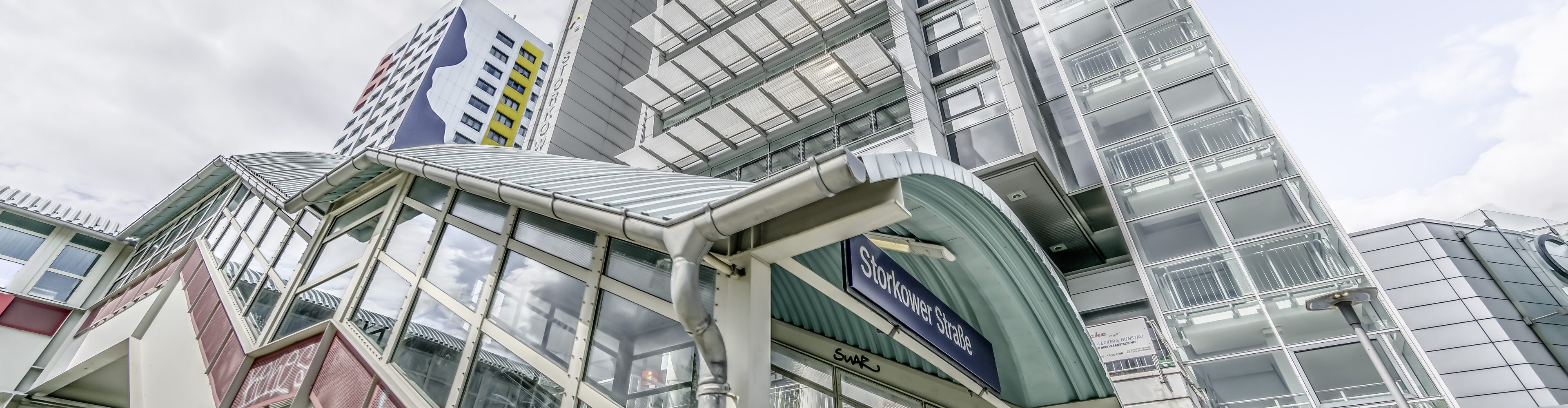 Ein Bild vom Treppenaufgang der S-Bahn-Haltestelle Storkower Straße, Berlin, Deutschland. Im Hintergrund ist ein buntes Hochhaus, sowie das Bürogebäude zu sehen, in dem die GEFEG mbH ihren Hauptsitz hat.