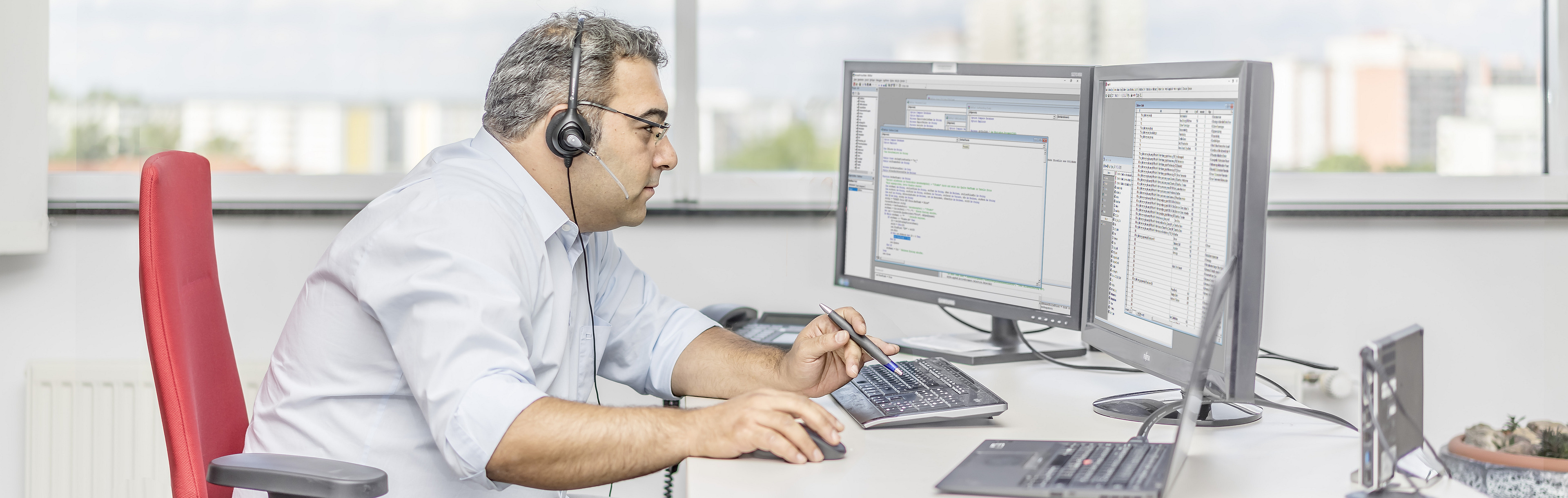 The picture shows a man with headphones, sitting at a desk in front of 2 screens and working with great concentration.