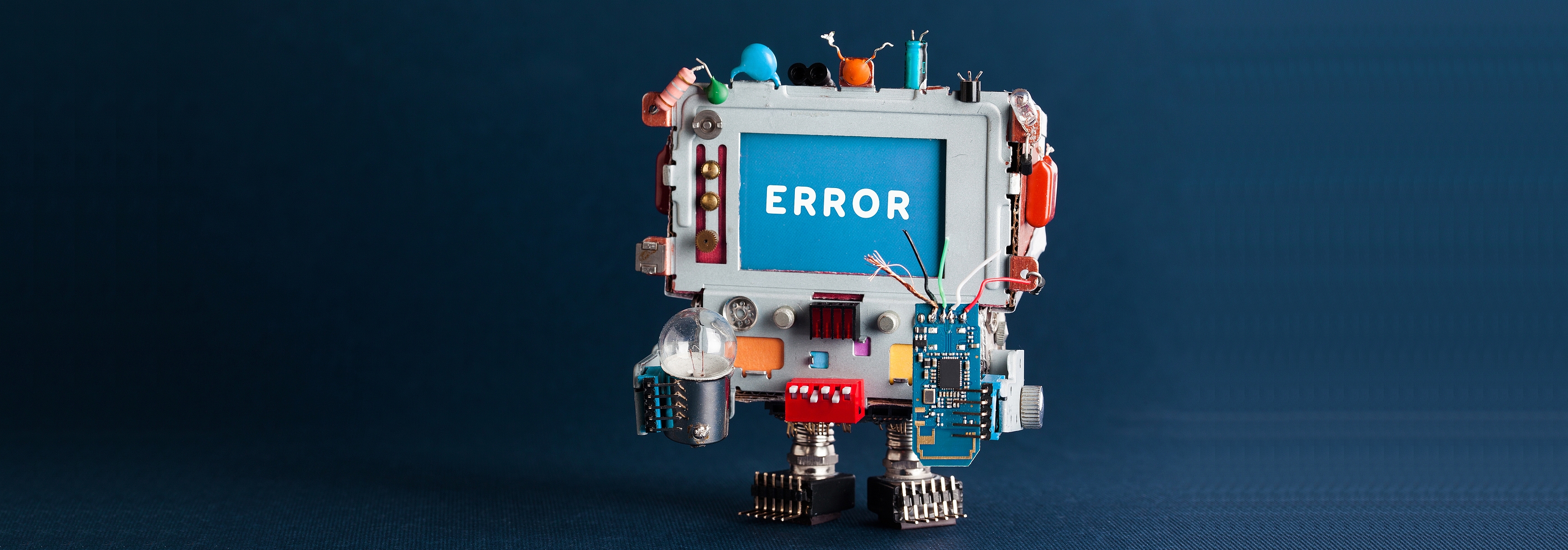 Spielzeug-Roboter-Computer mit Glühbirne und defektem Schaltkreis auf dunkelblauem Hintergrund, mit einem Kopf, der die Textmeldung Error auf blauem Bildschirm zeigt.